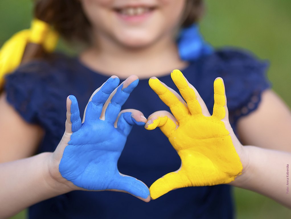Kind formt mit den Händen ein Herz, Hände sind blau und gelb eingefärbt