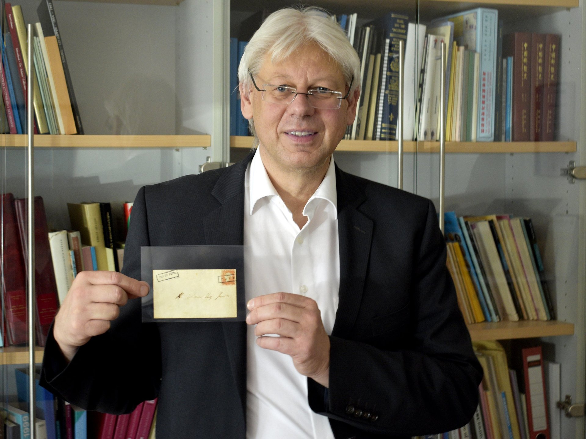 CEO Christoph Gärtner steht in seiner philatelistischen Bibliothek und hält freudestrahlend den Mauritius Ball Cover in Händen